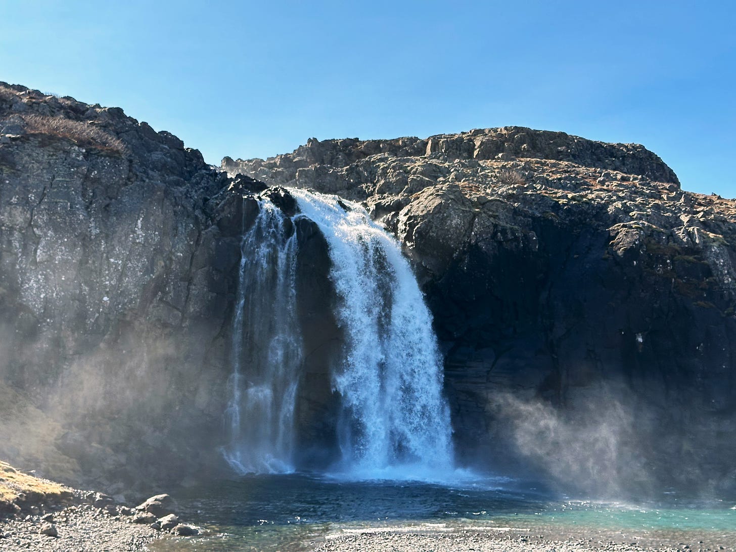 A beautiful waterfall flowing down from the rocky cliff behind the sheep farm.