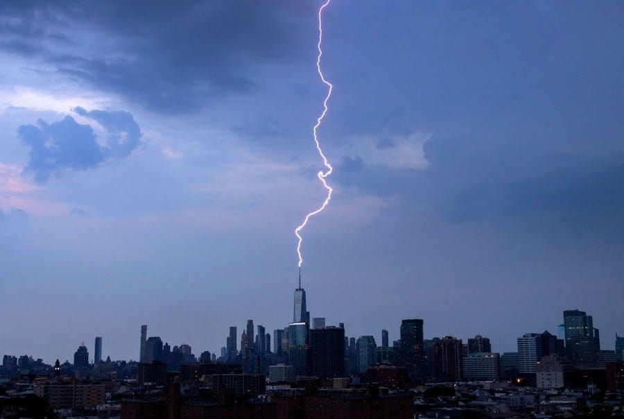 A lightning bolt strikes a tower atop a tall skyscraper in New York City.