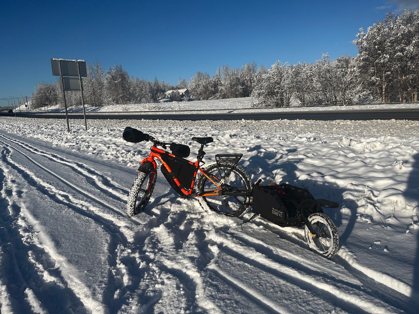 Orange fat tire bike parked in snow with a trailer and a deep blue sky