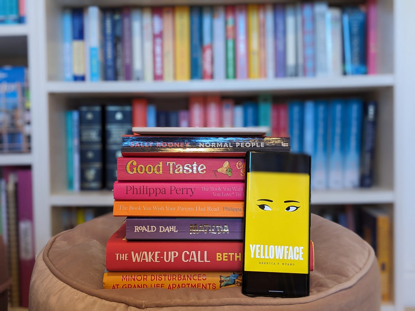 A pile of books, plus a phone propped up with Yellowface by Rebecca F.Kuang on the screen.