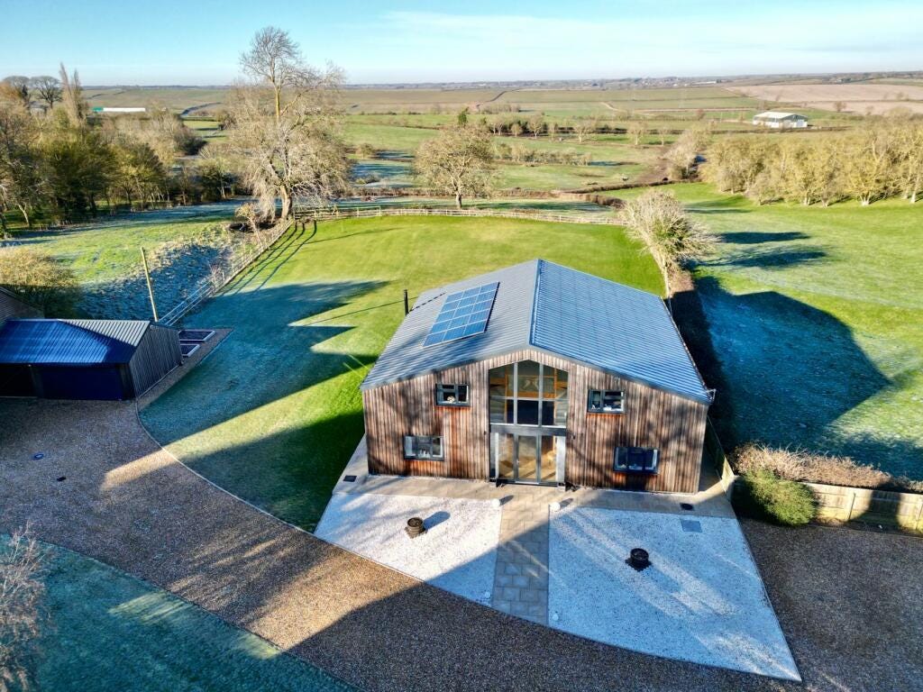 A large barn conversion looking house with gravel drive, large glass front and rolling hills and woods around it