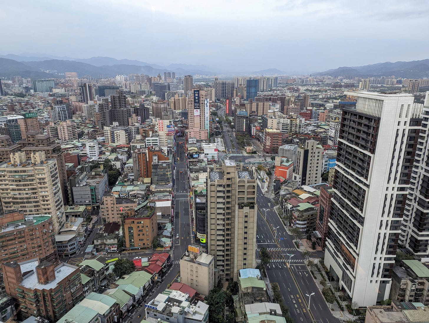cityscape with tall buildings and roads as seen from another tall building with mountains in the distance