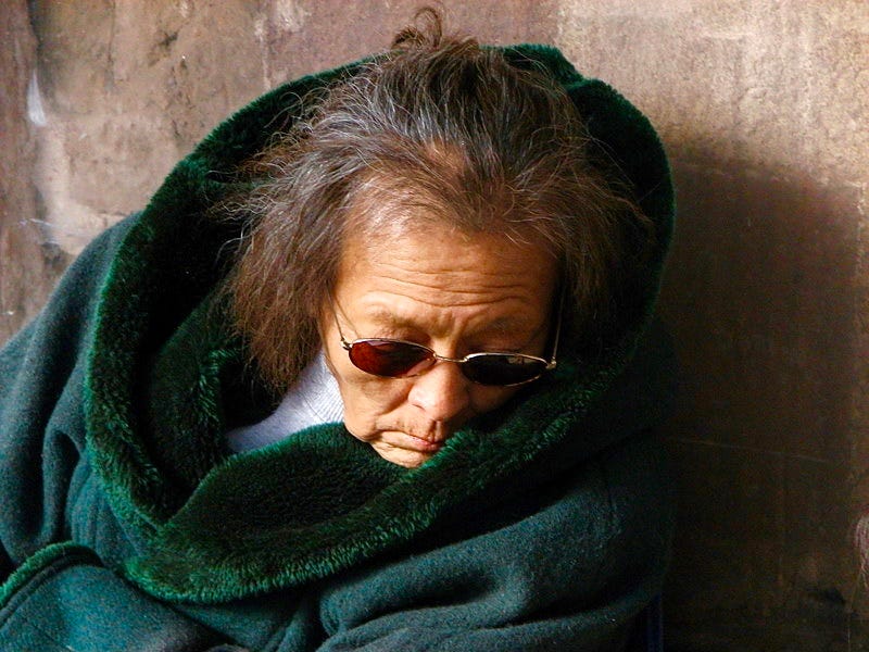A person wearing sunglasses and a green blanket

Description automatically generated