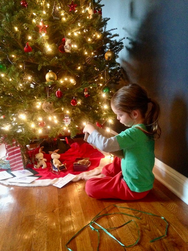 child sitting in front of Christmas tree reading a card