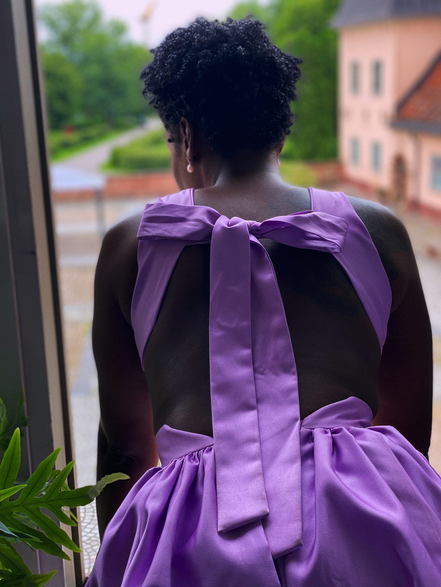 Lovette Jallow standing in lavender, turned away from the camera, facing a window. Caption: Lovette Jallow standing in lavender, turned away from the camera, facing a window. Caption: