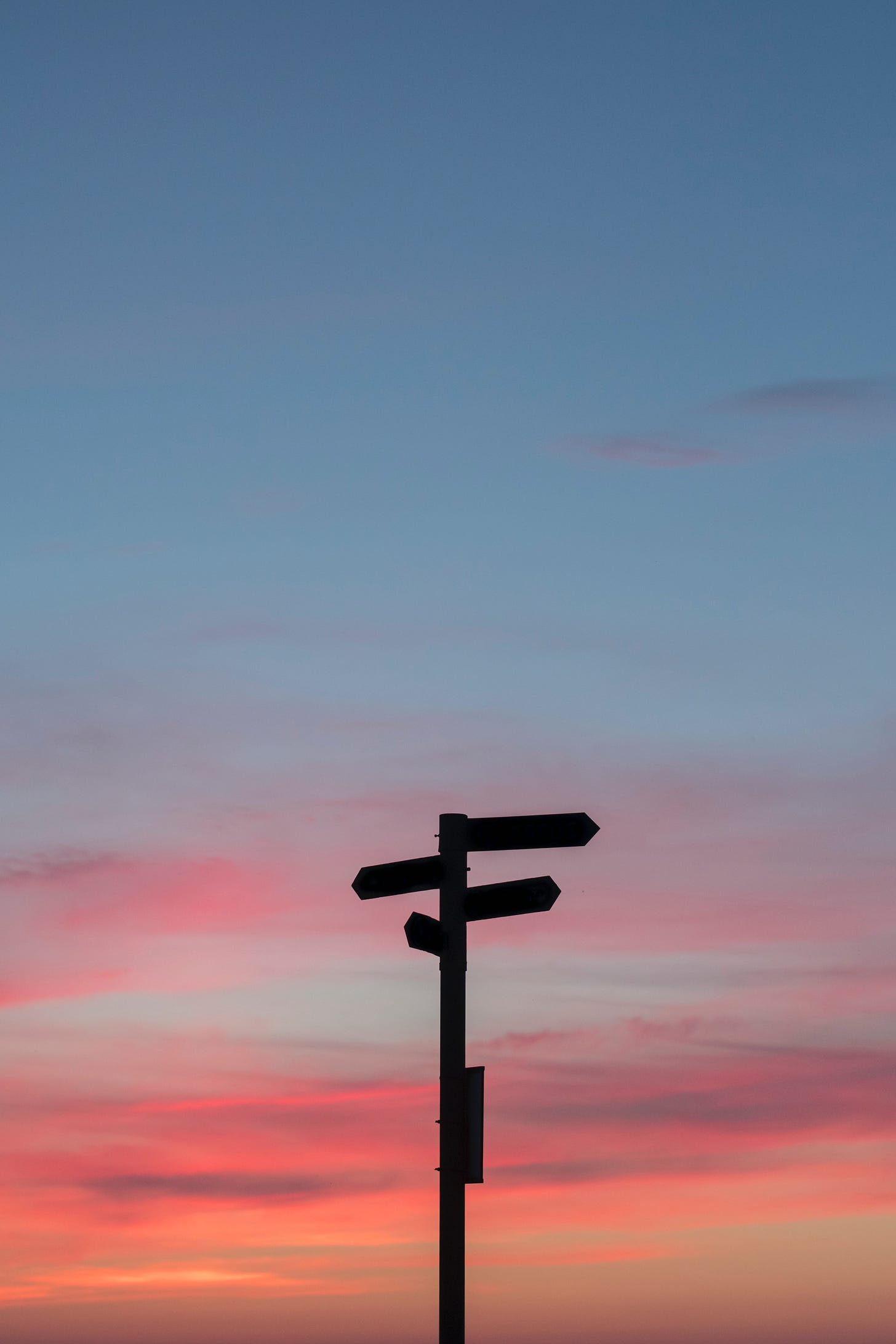 A beautiful pink and blue sky with a sign in silhouette that is pointing many directions.