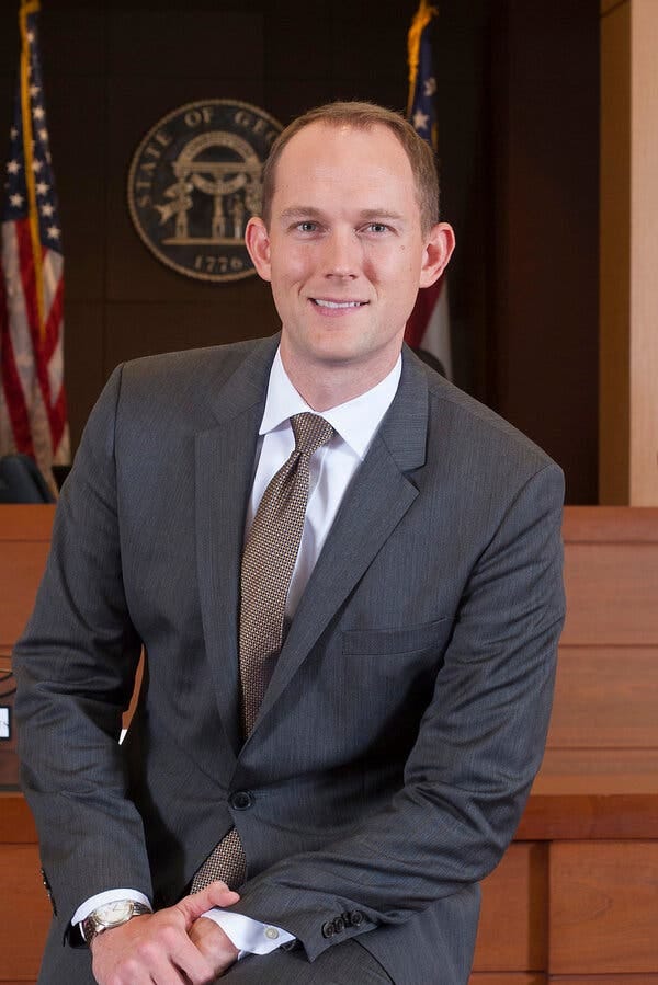 Judge Scott F. McAfee, in a suit and tie, poses for a portrait. The Georgia state seal is in the background.