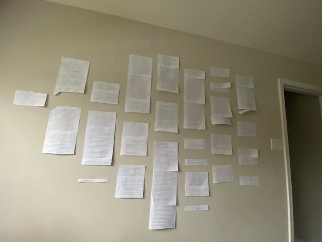 white pieces of paper cut into small sections of the essay, taped onto an off-white wall