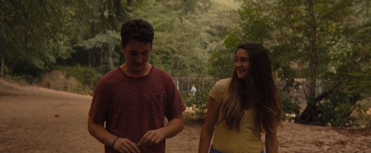 This may contain: two young people standing next to each other on a dirt road with trees in the background