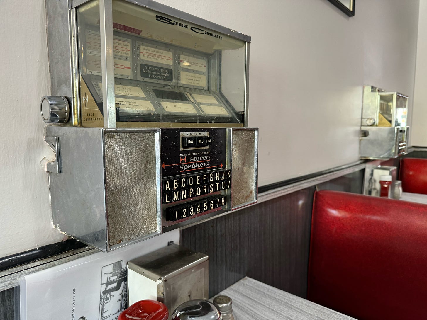 A Seeburg Consolette juke box mounted to the wall beside a booth