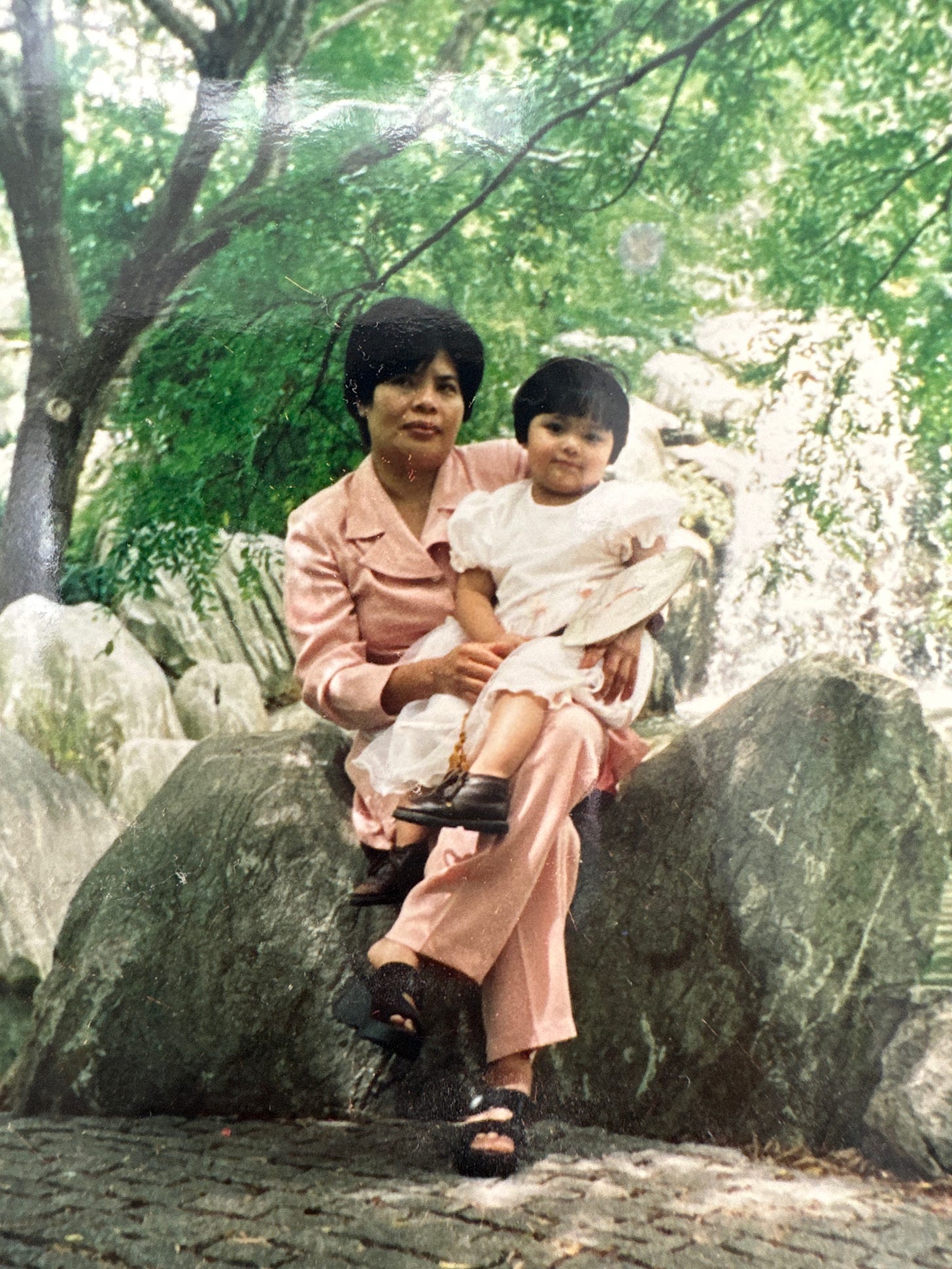 photo of Maggie as a toddler with her mother Kieu, sitting on a rock 