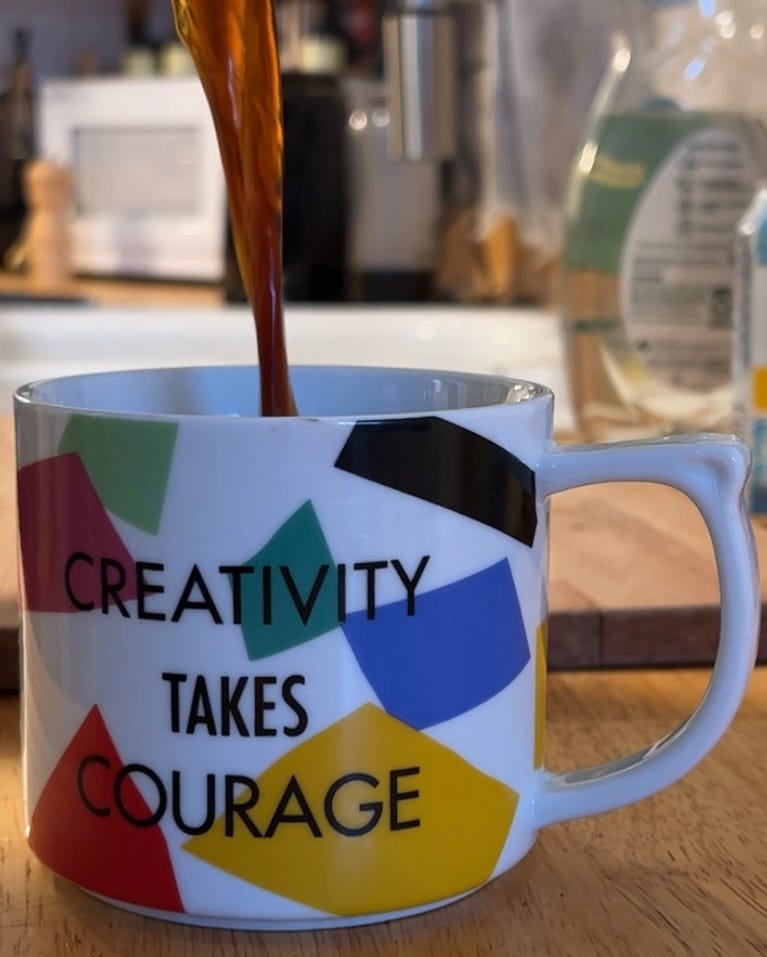 Coffee pours from out of the frame into a white mug with rectangular blocks of color and a quote attributed to Henri Matisse that reads Creativity Takes Courage
