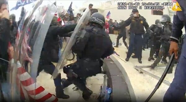 A time-stamped frame grab from a video shows a man in a black jacket using both hands to push against a U.S. Capitol Police officer’s shield. 