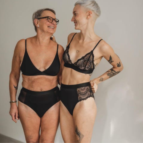 Una donna over 50 e una donna tatuata in intimo nero, di pizzo. I loro corpi non sono stati ritoccati, quindi hanno rotoli e smagliature come è naturale che sia