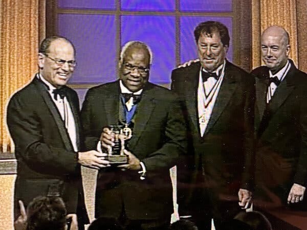 Joseph Neubauer, Justice Clarence Thomas, Paul Anthony Novelly and David Sokol stand in a line, all wearing tuxedos, the justice holding an award.
