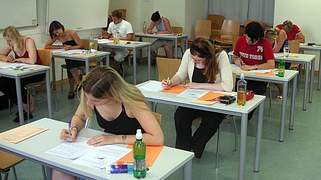 Nine college-age students at individual desks taking an exam.