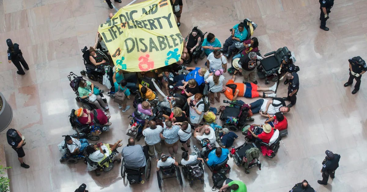 A photo shot from above of disabled activists on the shiny floor of a US Capitol building. Many are wheelchair users. There is a sign that says Medicaid = Life + Liberty 4 Disabled.