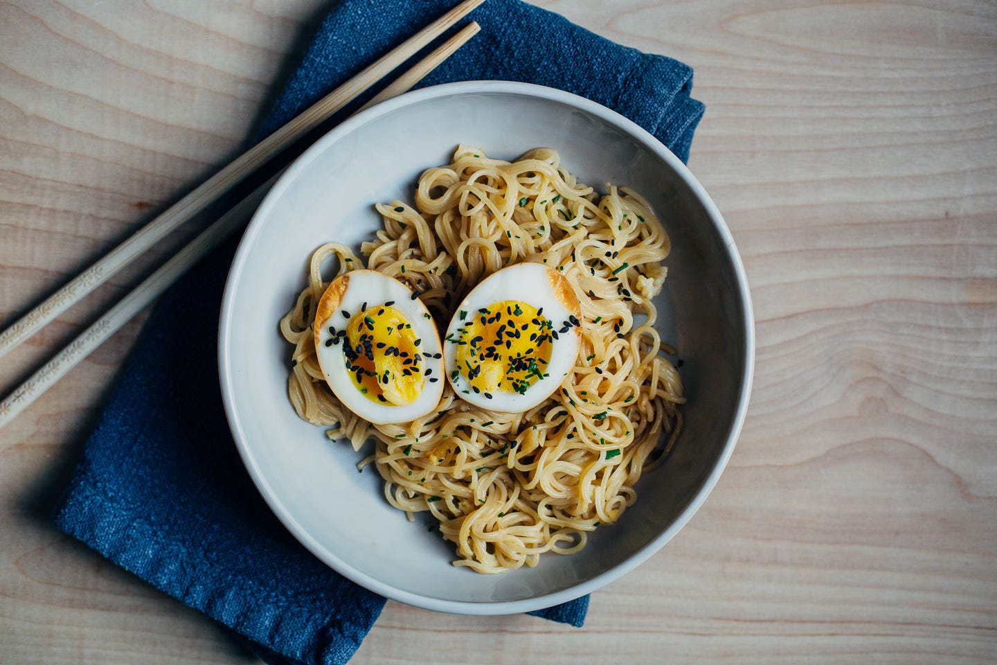 A bowl with soy sauce eggs atop ramen noodles with a napkin and chop sticks alongside. 