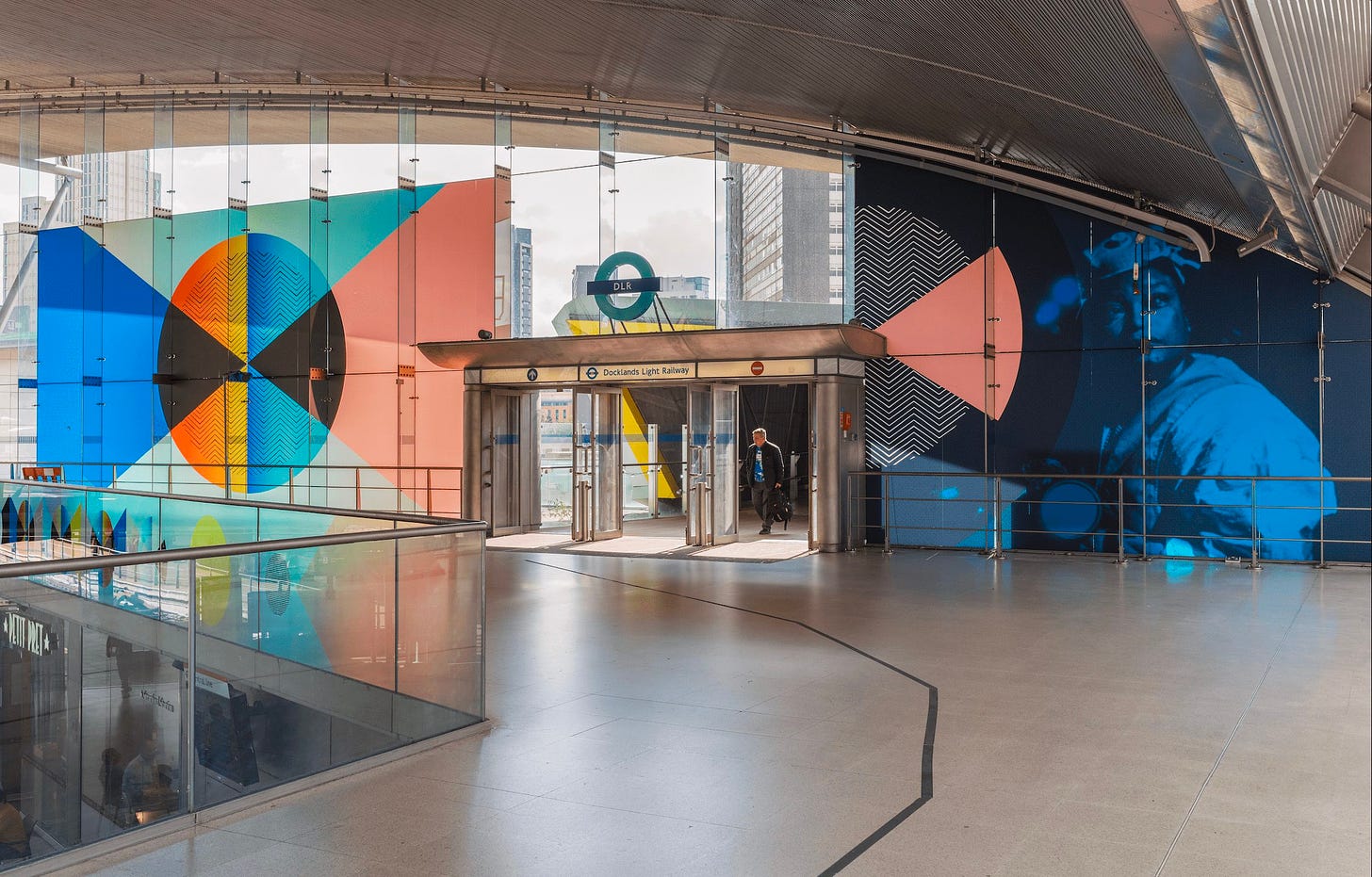 Artwork mounted on glass showing overlapping peach, blue black geometric shapes in a metro station.