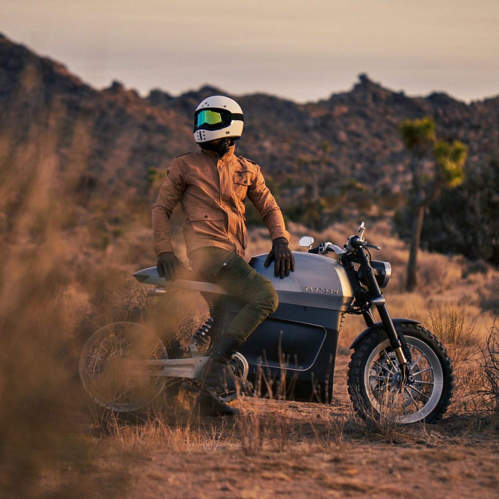 A Tarform Luna electric motorcycle with rider atop on a dirt terrain.