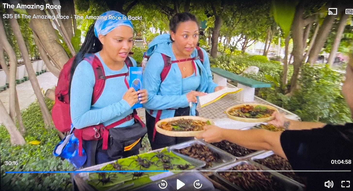 Image from CBS's The Amazing Race showing two contestants being handed plates of bugs to eat.