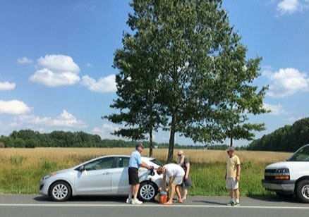 A group of people rescuing a car out of gas by the side of the road.