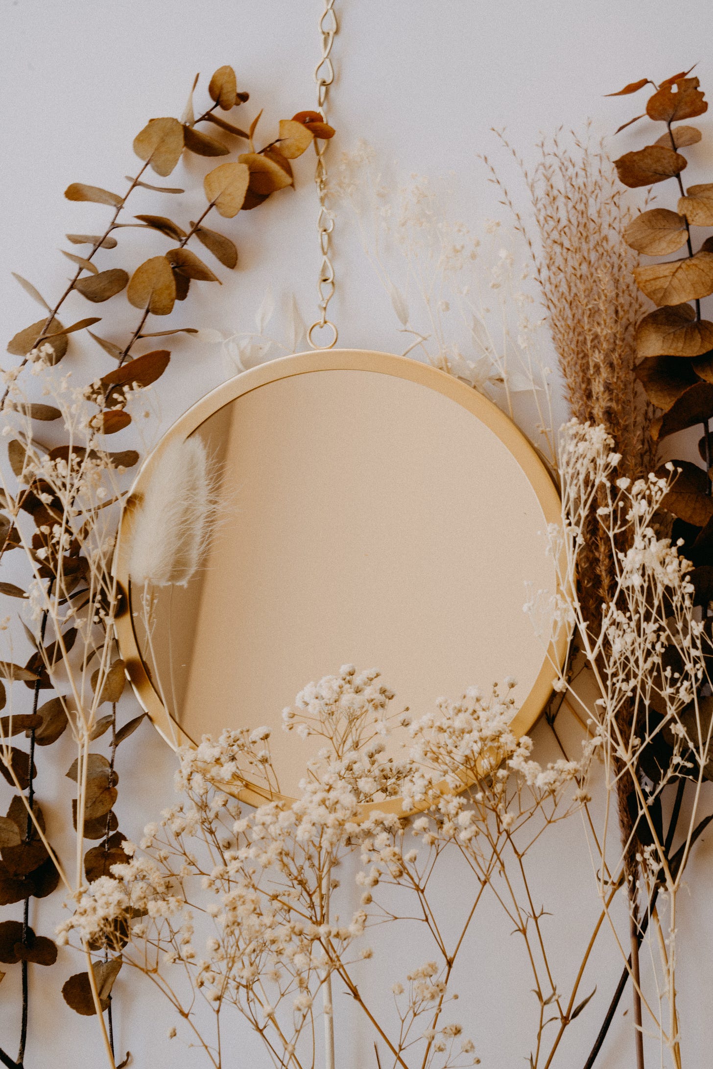 Rustic gold mirror with dried plants around it. Reflection