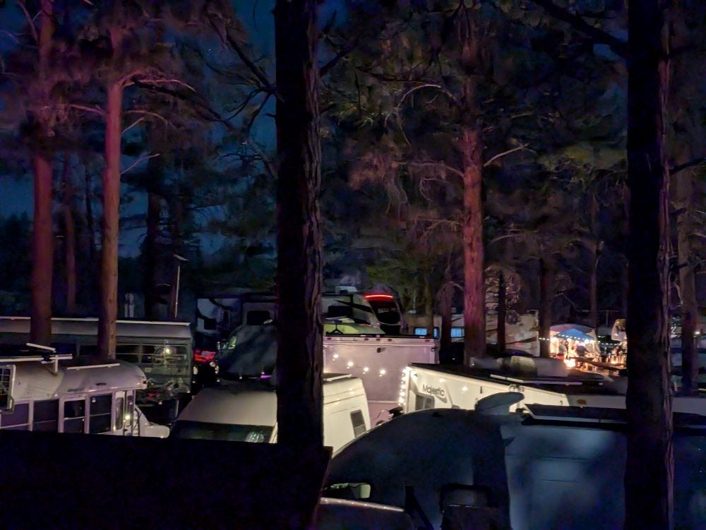 a rooftop view of a crowded campground at night, vans and buses and campers set amongst the pine trees