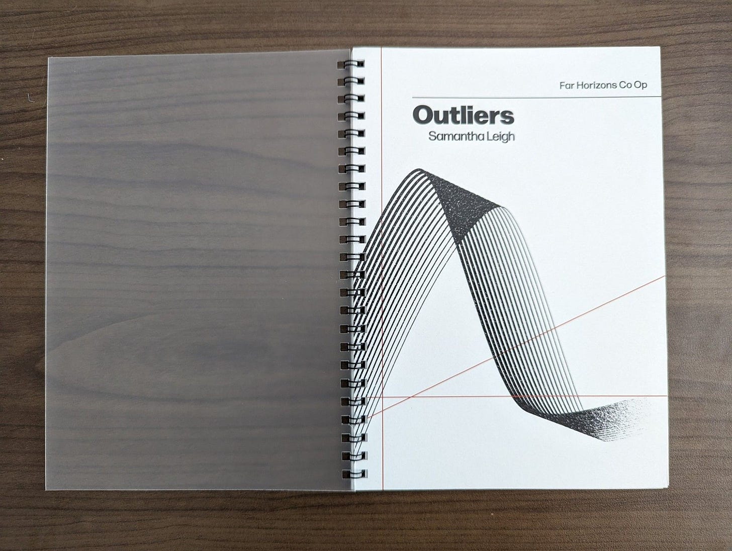 A printed copy of Outliers, which is spiral-bound with a frosted cover
