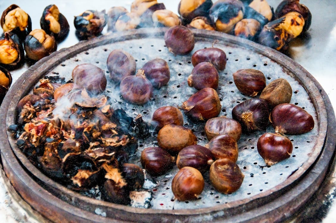 Free Close-up view of roasted chestnuts smoking on a round grill, emphasizing texture and warmth. Stock Photo