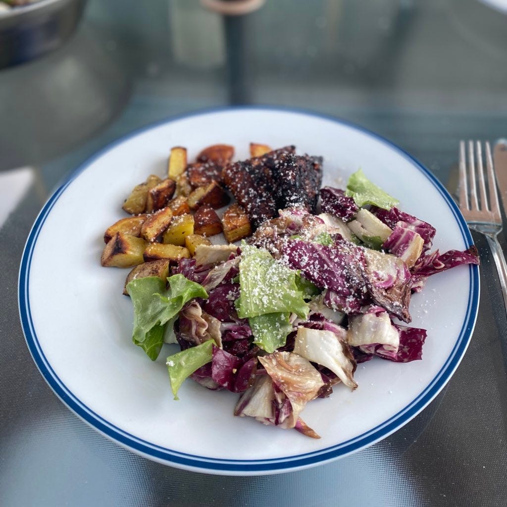 Potatoes, tempeh, and a radicchio and green lettuce caesar on a dinner plate, all dusted with parmesan.