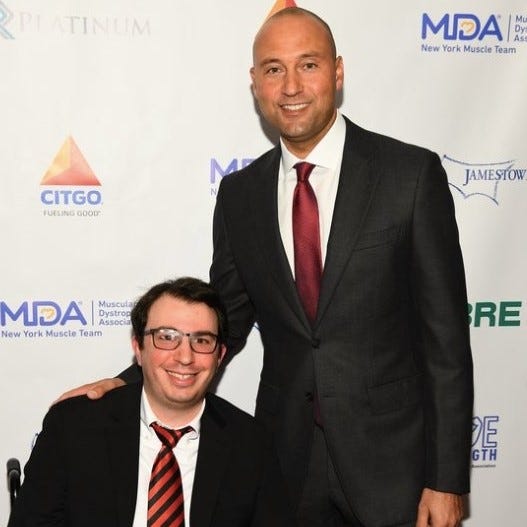 Author taking a picture with Derek Jeter. Jeter is standing, author is sitting. Both are wearing a suit.