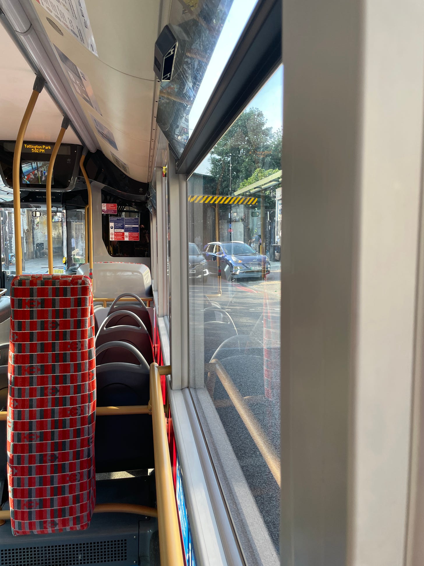 The inside of a single-decker bus with a bit visible outside the window that has a low bridge warning.