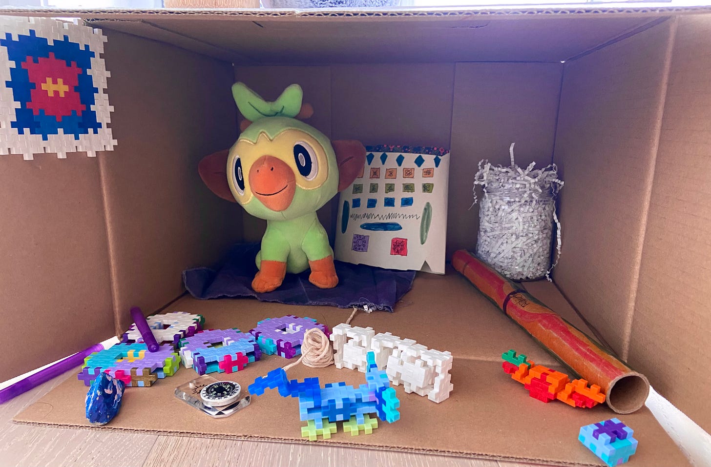 Grookey pokemon stuffed animal in cardboard box with other objects laid out like wares in a shop