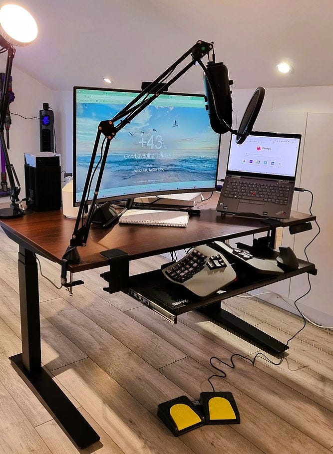 Computer workstation with foot pedal, ergonomic keyboard, mouse, under desk tray, boom stand mic, and soft spotlight.