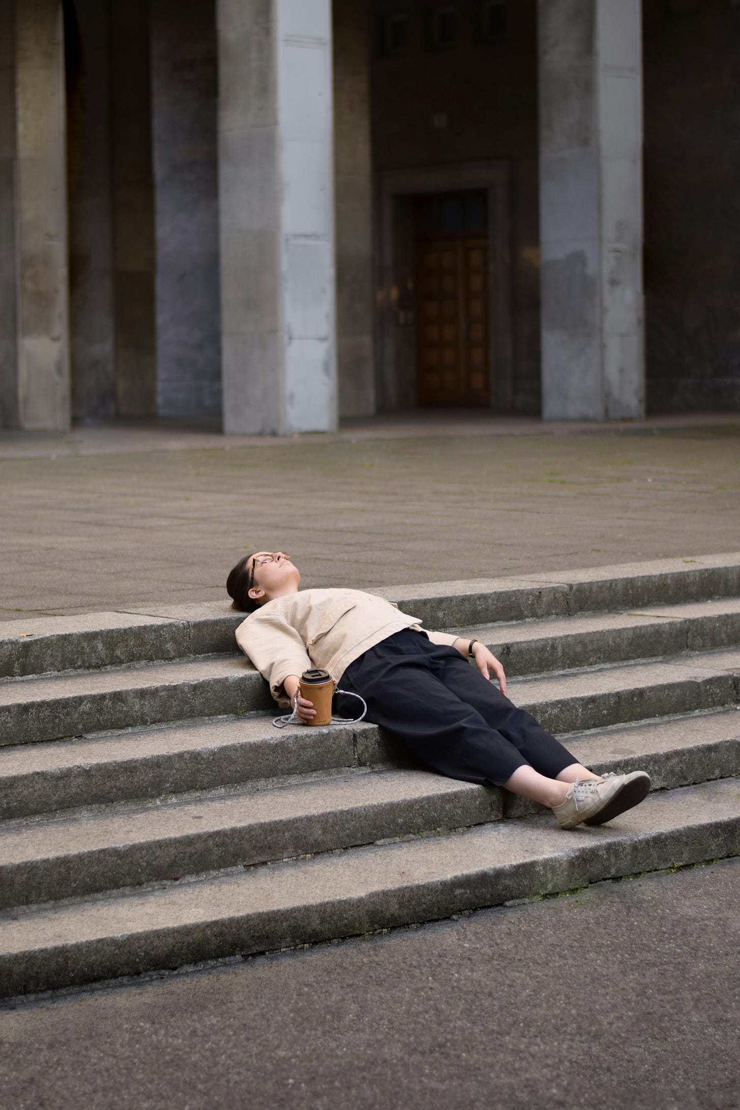 A person lying down on their back on some steps. They have their eye closed and they look exhausted.