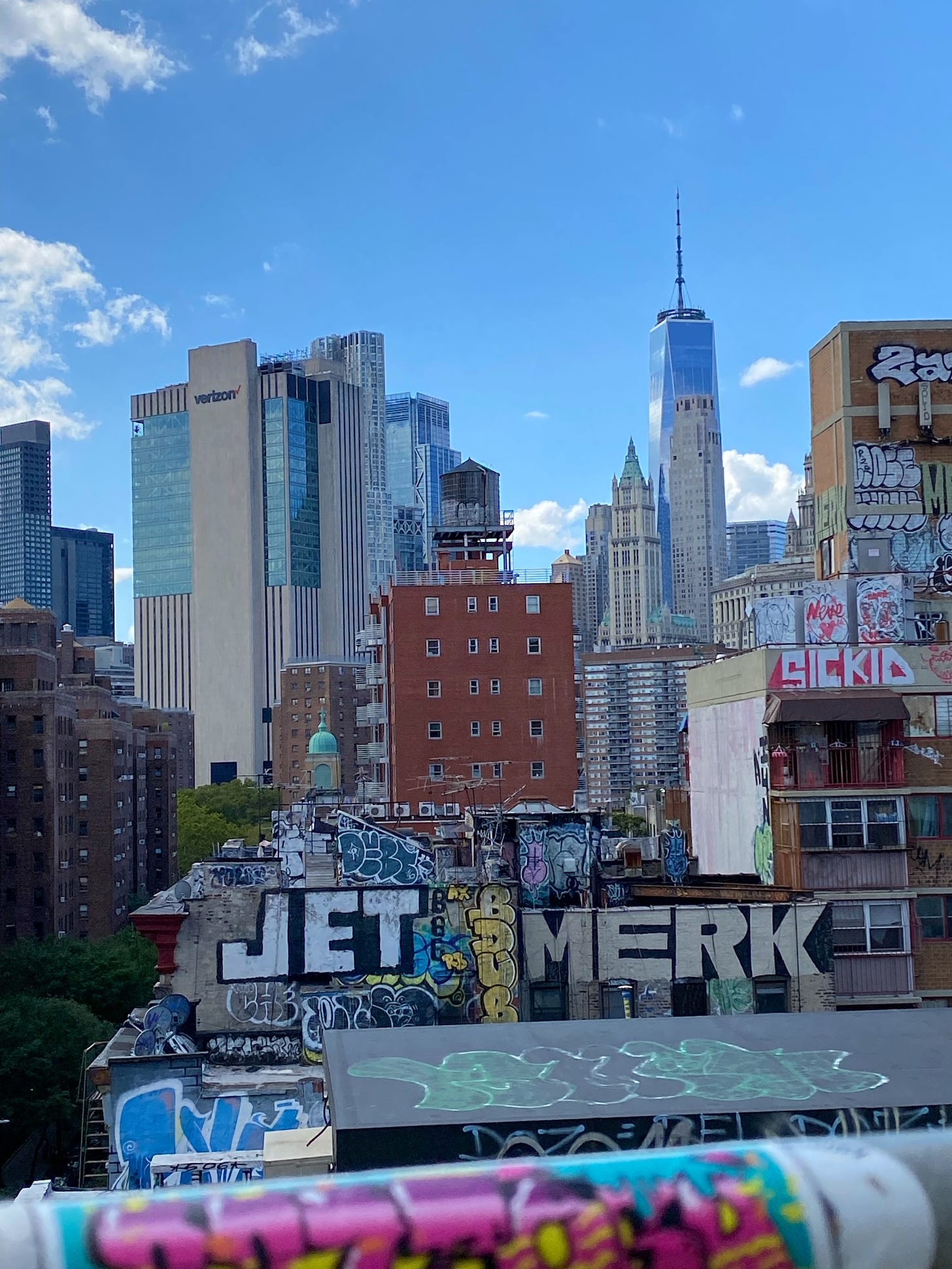 A gray water tower stands on a heavily tagged roof. Behind it are ranged the lowers of lower Manhattan, the Trade Center tallest.