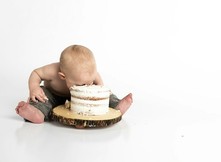 A hungry baby eats a cake.