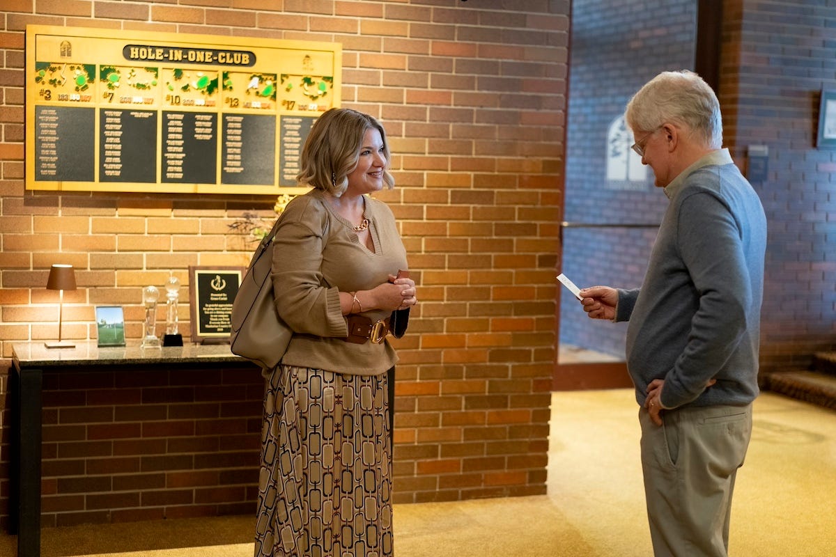 Mary Catherine Garrison is pictured wearing a beige top and skirt speaking to an older gentleman at a country club on the set of Somebody Somewhere