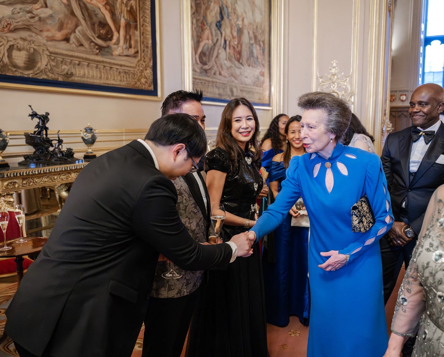 Princess Anne wearing a blue dress shaking the hand of a bowing man in a suit