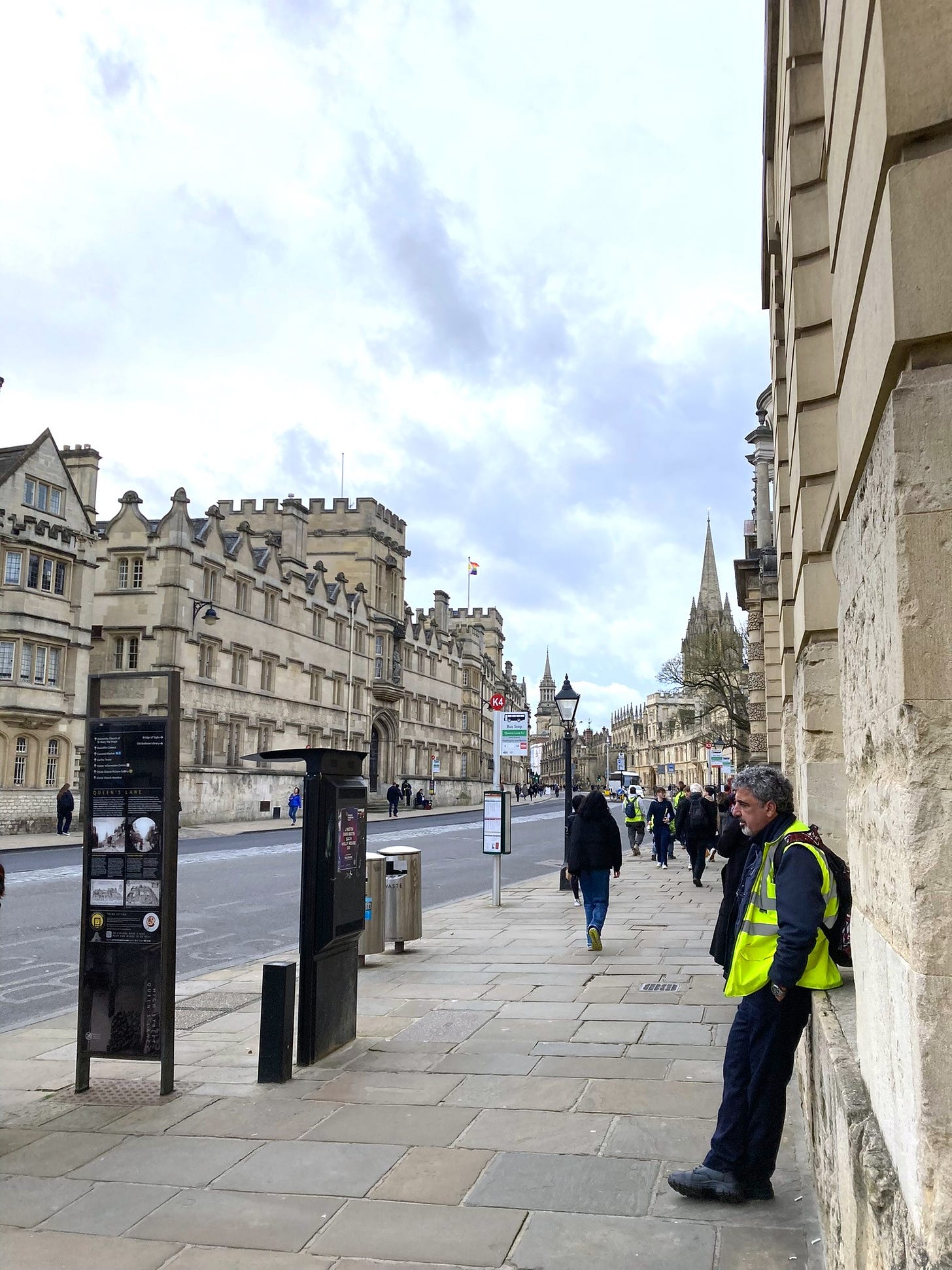 The creamy building of Oxford high street against a blue cloudy sky. A man in a high-vis jacket is in the foreground.
