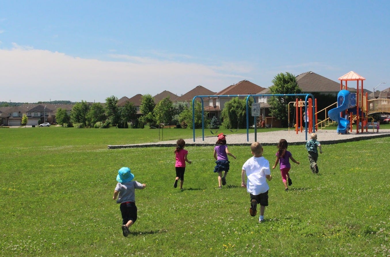 Photograph of several small children running toward a play structure at a park on a sunny day