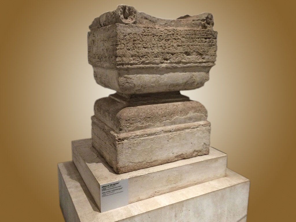 A large stone object with faded Greek writing imprinted on it against a brown background, the original "altar to an unknown God" from the book of Acts