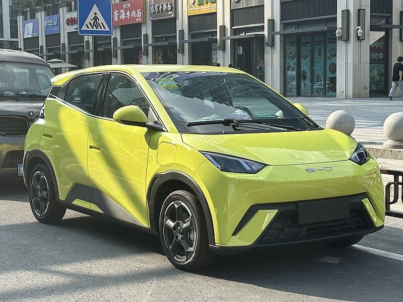 A small yellow-green 4-door  compact electric car, the BYD Seagull