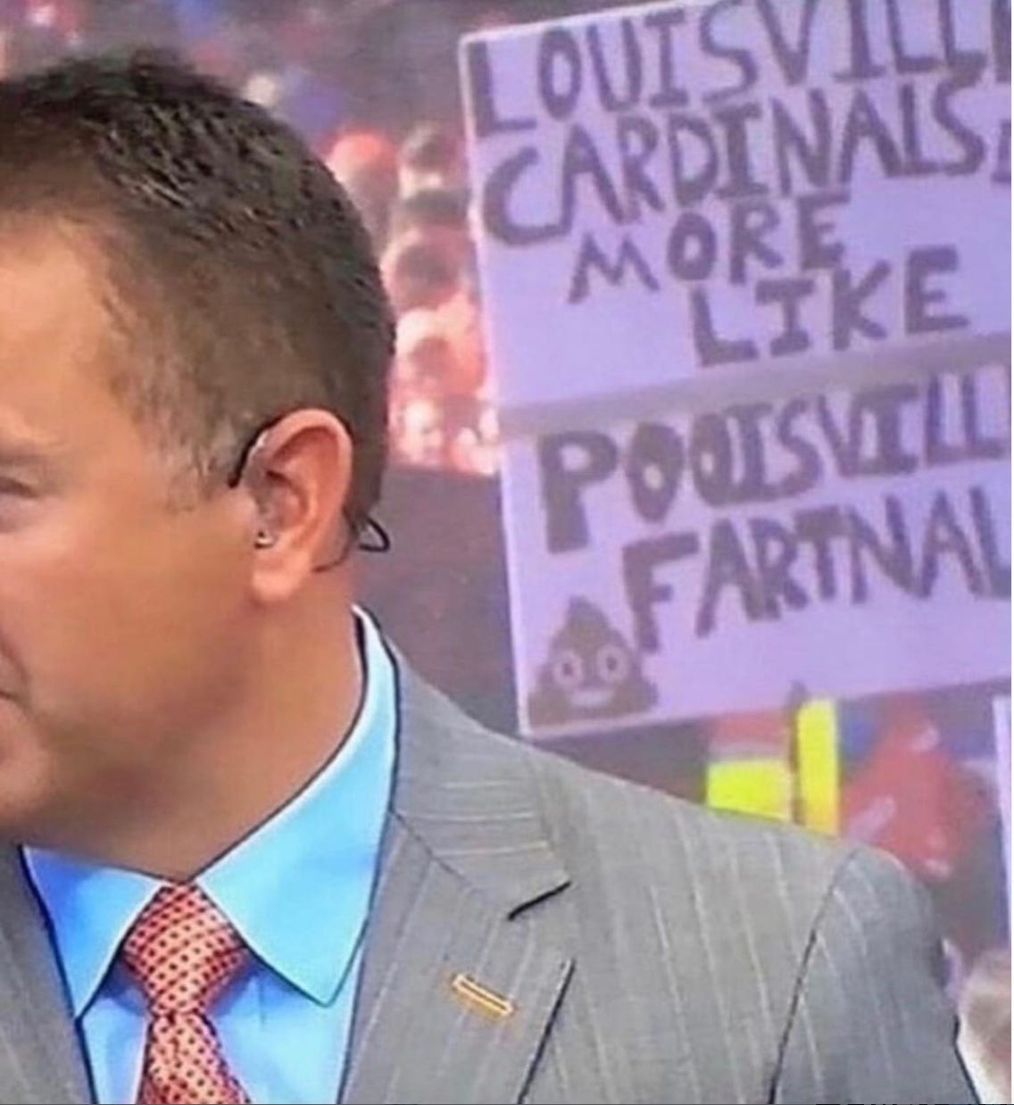 A bad snapshot of a TV screen showing a sportscaster with a fan sign in the background that reads LOUISVILLE CARDINALS? MORE LIKE POOISVILLE FARTNALS