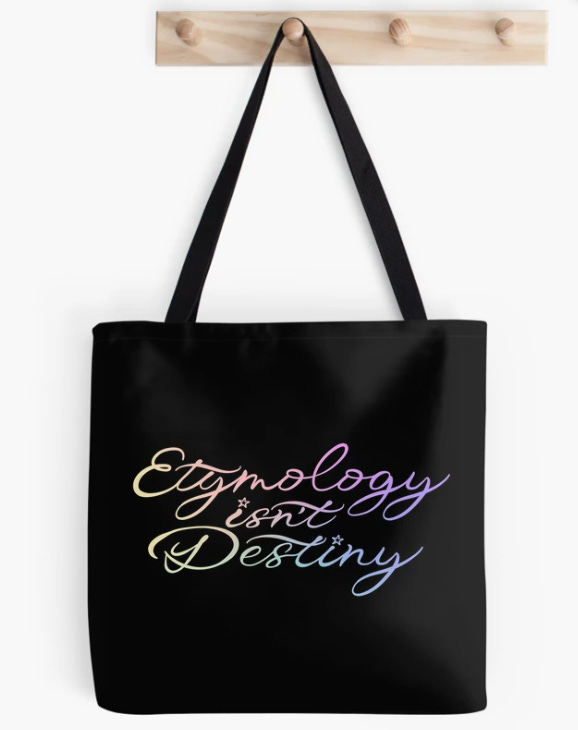 "Etymology isn't destiny" in swoopy rainbow gradient text on a black tote bag hanging from a wooden hook.