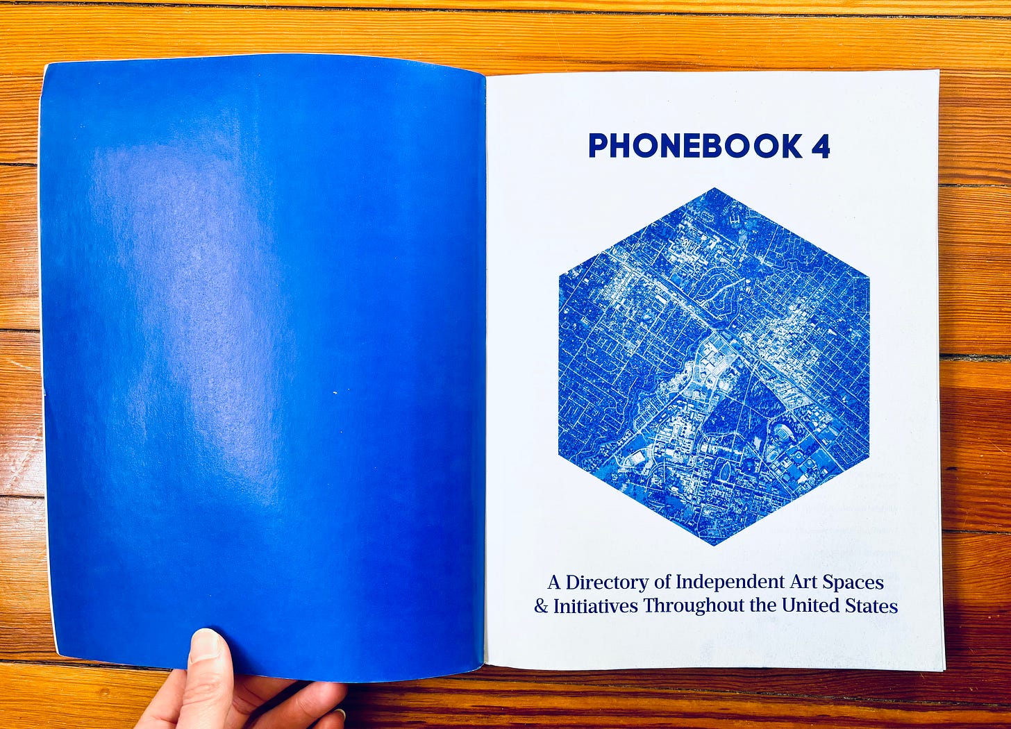 a photo of a large book with an all-blue left page and a right page that says PHONEBOOK 4 with an octagonal shape filled with a map illustration a photo of a large book with an all-blue left page and a right page that says PHONEBOOK 4 with an octagonal shape filled with a map illustration