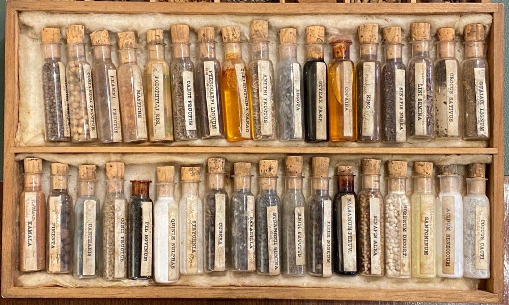 A wooden case containing two rows of small, slim corked bottles, each containing a sample of a botanical medicine. They are labelled with the name of the contents.
