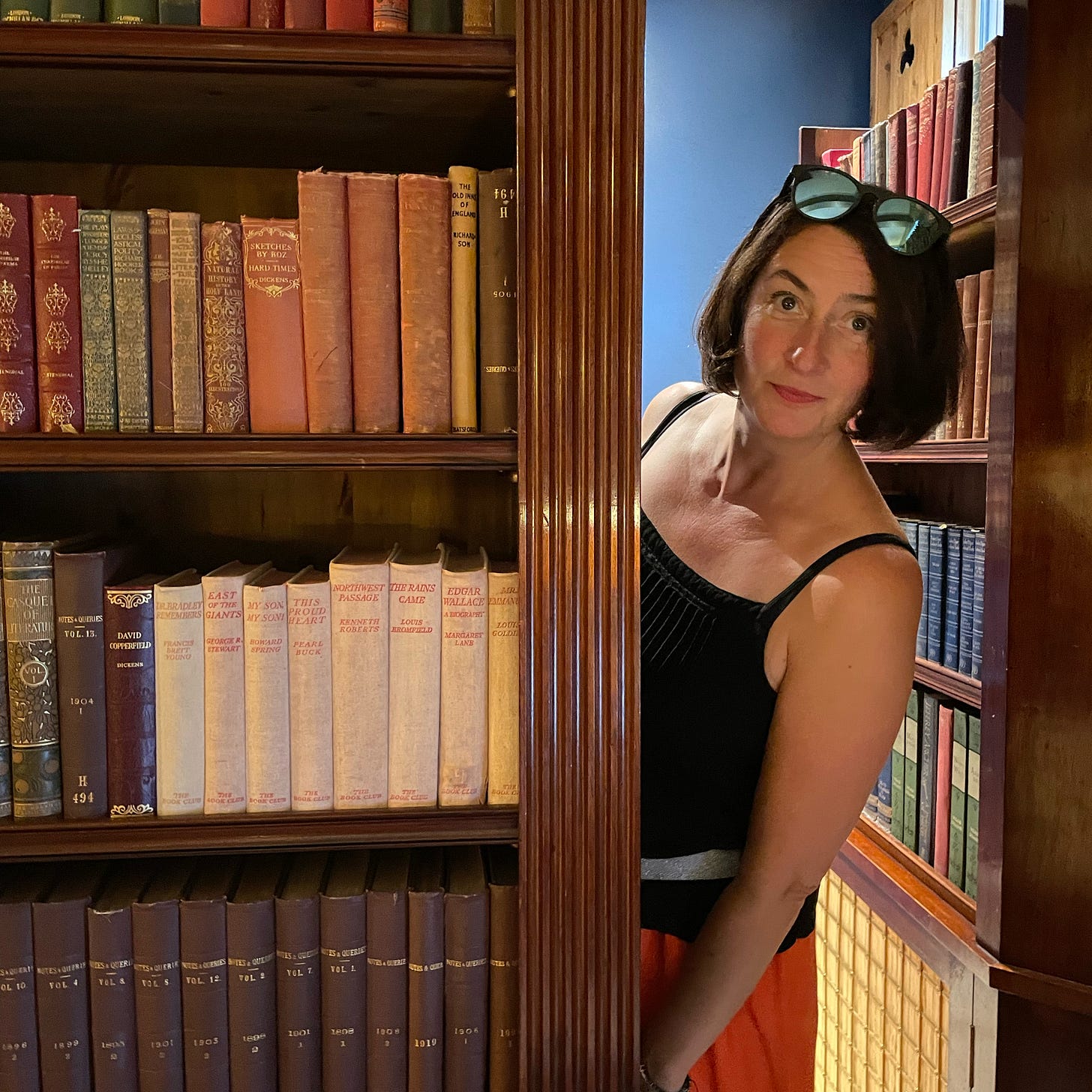 Sarah Farley peeks her head around a book shelf with lots of old hardback books on it