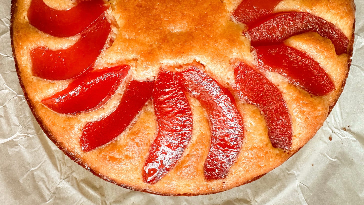 A closeup photo of a round cake topped with slices of pink poached quince.